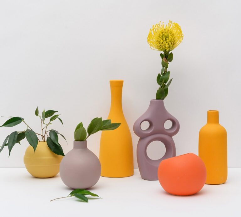 Group of colorful matte ceramic vases with plants arranged on a white surface yellow lavender gray on a clean backdrop