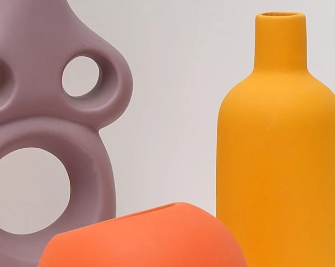 Abstract still life lavender silicone sculpture with circular holes an orange bottle and a coral block against a pale background